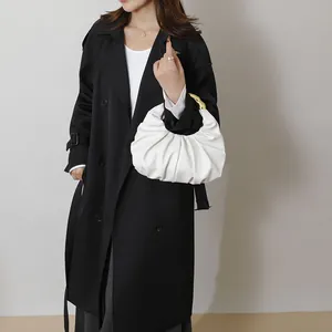 White ruched cloud handbag with round gold metal handle shown on a black trench coat