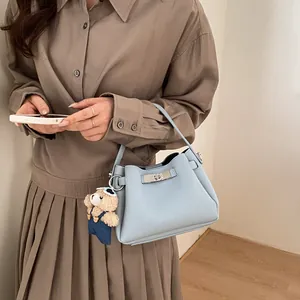 Detail of light blue lychee pattern leather handbag with silver clasp and cute bear charm