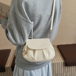 Détail du sac selle plissé blanc cassé avec anneau doré et logo de mode élégant