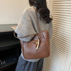 Detail of vintage brown leather tote bag featuring a colorful wooden bead charm and logo