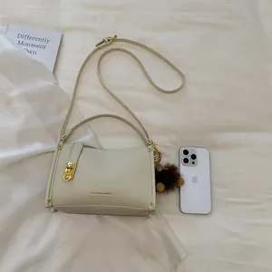 Detailed macro view of a cream leather Boston bag with gold buckle and plush bear charm