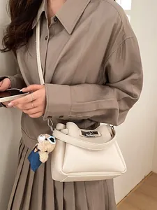 Chic beige crossbody bucket bag with litchi texture and cute bear charm shown on model