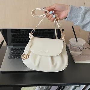Vue détaillée du sac besace crème avec base plissée et boucle dorée en décor quotidien