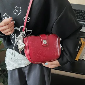 Detail of red saddle bag in glossy wrinkled leather with silver heart charm and buckle