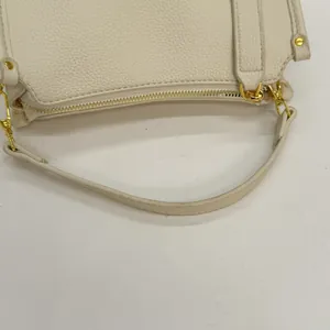 Close-up of cream white lychee leather texture with gold metal zipper and strap