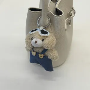 Dettaglio di un portachiavi a forma di cane in peluche beige con occhiali blu