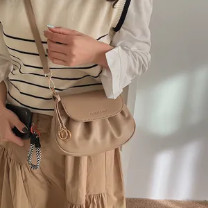 Détail du sac bandoulière plissé kaki avec anneaux dorés et logo imprimé sur le rabat