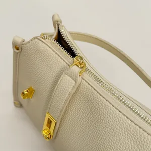 Close-up of litchi grain cream leather Boston bag featuring luxury gold zipper hardware