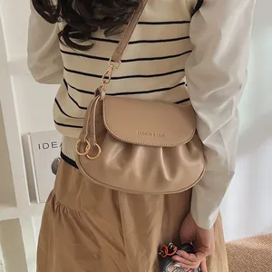 Détail d'un sac selle beige plissé avec breloques dorées et lettrage de mode
