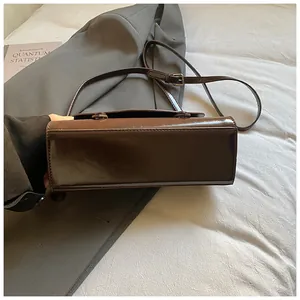 Detailed side view of a brown glossy PU leather shoulder bag with adjustable strap