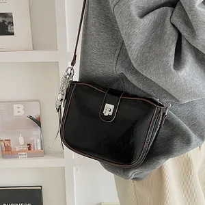 Detail of black glossy saddle bag with silver twist lock and brown shoulder strap