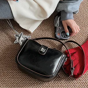 Detail of black glossy saddle bag with silver buckle and star charm on woven mat