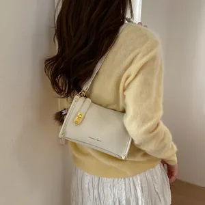 Detail view of cream lychee leather handbag with gold lock and brown plush charm