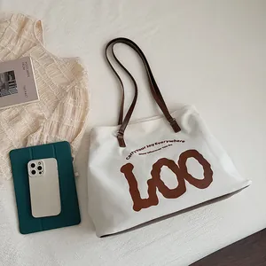Detailed front view of white canvas tote bag with brown straps and typography print