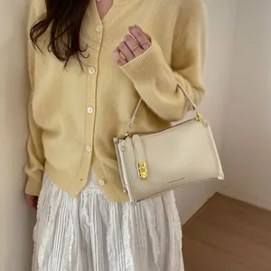 Close-up of minimalist cream Boston bag with litchi texture and golden metal lock detail