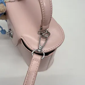 Nahaufnahme der rosa Box-Tasche mit Silberverschluss und blauem Plüsch-Puppenanhänger