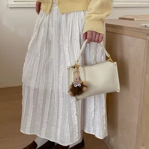 Detail of a creamy white pebbled leather handbag with a brown plush monster charm