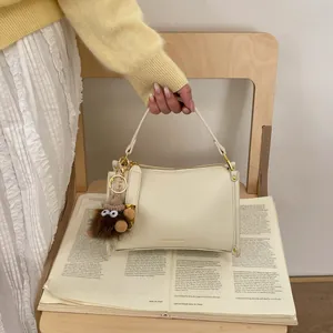 Close-up of cream Boston bag with lychee texture and a brown plush monster charm