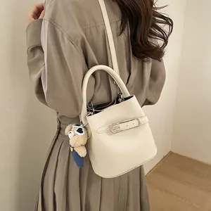 Dettaglio di una borsa a secchiello bianco crema con trama martellata e ciondolo a orsetto