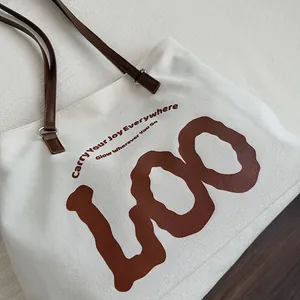 Detail of leather handles and artistic printed lettering on a canvas tote bag