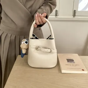 Dettaglio borsa a secchiello in pelle beige con fibbia argento e ciondolo orsetto