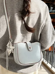 Light blue saddle shoulder bag with wavy top and star leaf charm on grey sweatshirt