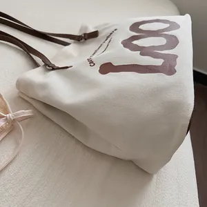 Close-up of canvas tote bag texture with brown LOO print and adjustable leather strap