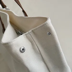 Detail of canvas tote bag showing cream fabric texture, silver snap button, and leather handle