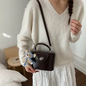Details einer dunkelbraunen Box-Tasche mit Drehverschluss, Schultergurt und Bärenanhänger