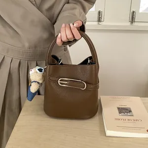 Dettaglio della borsa a secchiello marrone con trama litchi e ciondolo a orsetto
