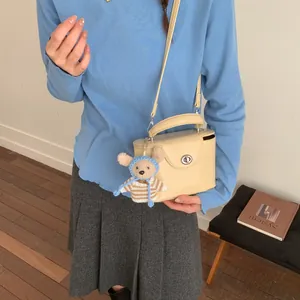 Detailansicht beige Box-Handtasche mit Metalldrehschloss und süßem Bärenanhänger