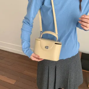 Detail der cremegelben quadratischen Handtasche mit silbernem Drehverschluss und Schultergurt
