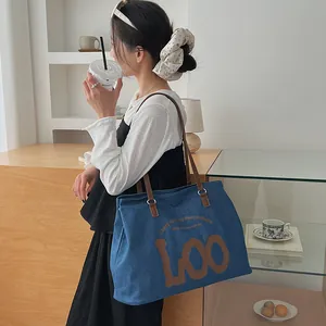Detail of blue denim tote bag with leather straps and printed logo for daily use