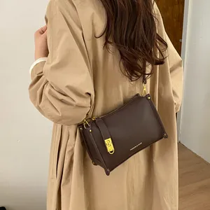 Close-up of a brown leather Boston bag with gold buckle and embossed fashion logo text