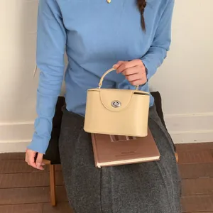 Detail einer beigefarbenen Kofferhandtasche mit silbernem Drehverschluss und glattem Leder