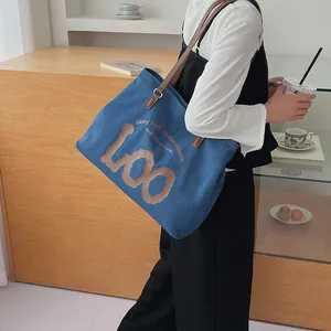Close-up of blue denim tote bag with leather strap and decorative LOO print