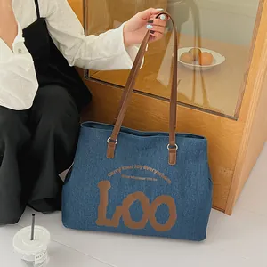 Detail of blue denim tote bag with brown leather straps and stylish printed letters