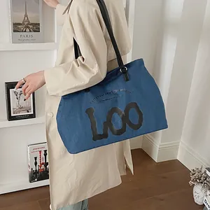 Detail of blue denim tote bag with black leather straps and stylish LOO art lettering