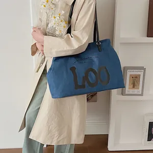 Detailed shot of large blue denim tote bag with black leather straps and LOO art print