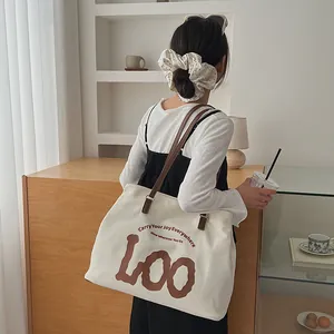 Detail of canvas tote bag with brown leather straps and printed joy slogan