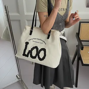 Lifestyle shot showing a large white canvas tote bag with black LOO lettering and straps