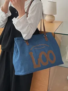 Denim tote bag with brown leather straps and artistic lettering shown in a lifestyle setting
