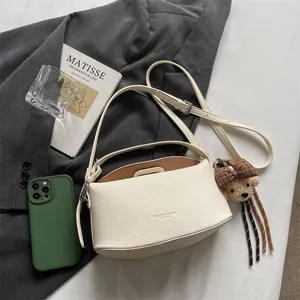 Gros plan du sac à main blanc en cuir grainé avec un porte-clé ours sur une veste grise