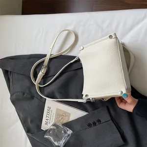 Detailed view of a white lychee grain square crossbody bag with silver rivet accents
