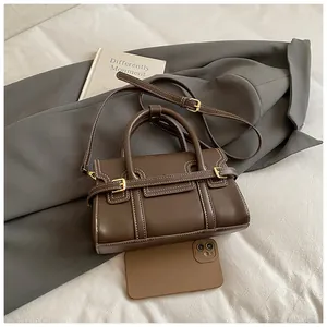 Detail of dark brown leather handbag with white contrast stitching and gold metal buckles