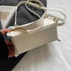 Detail of cream crossbody bag showing pebble grain texture and silver metal rivets
