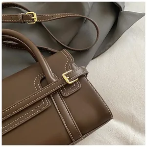 Close-up of deep brown leather bag showing white contrast stitching and gold buckle