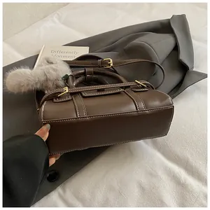 Detail of dark brown leather handbag featuring contrast stitching and a fuzzy ball charm