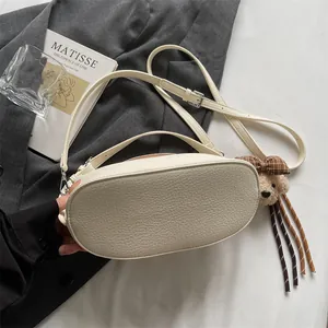 Détail du sac à main en cuir grainé blanc crème avec un charm ours sur costume gris
