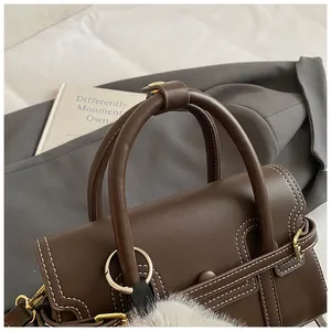 Detail of dark brown vintage handbag with contrast white stitching and plush charm